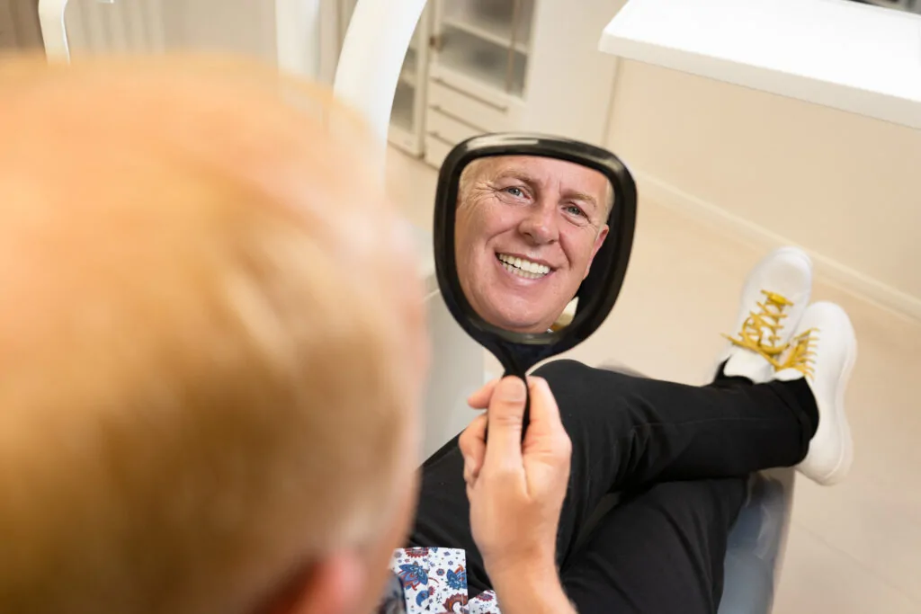 Patient schaut sich seine Zähne in einem kleinen Spiegel an.