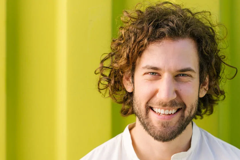 Mann mit Zahnarztangst lächelt vor grünem Hintergrund.