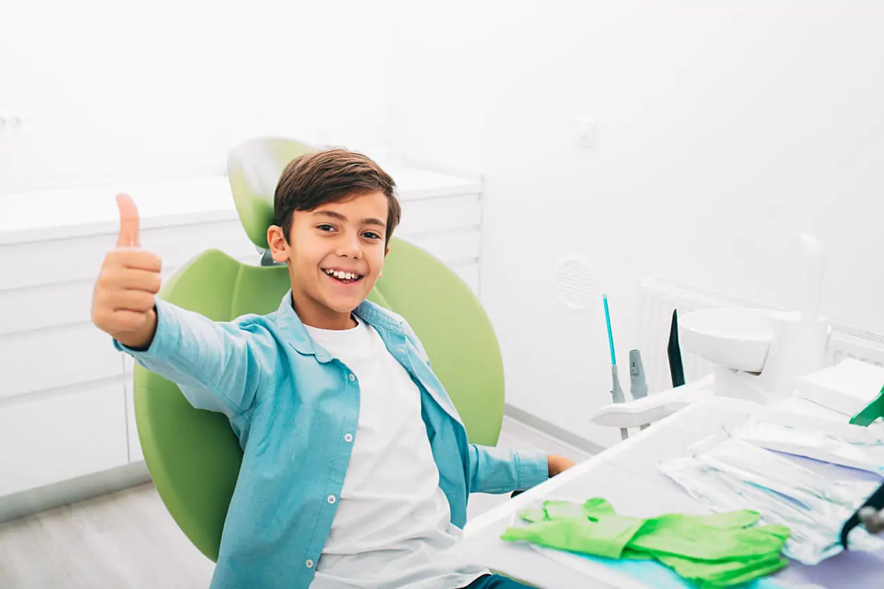 Kind sitzt auf Zahnarztstuhl und hebt Daumen hoch nach Behandlung als Angstpatient bei Dr. Henninger.