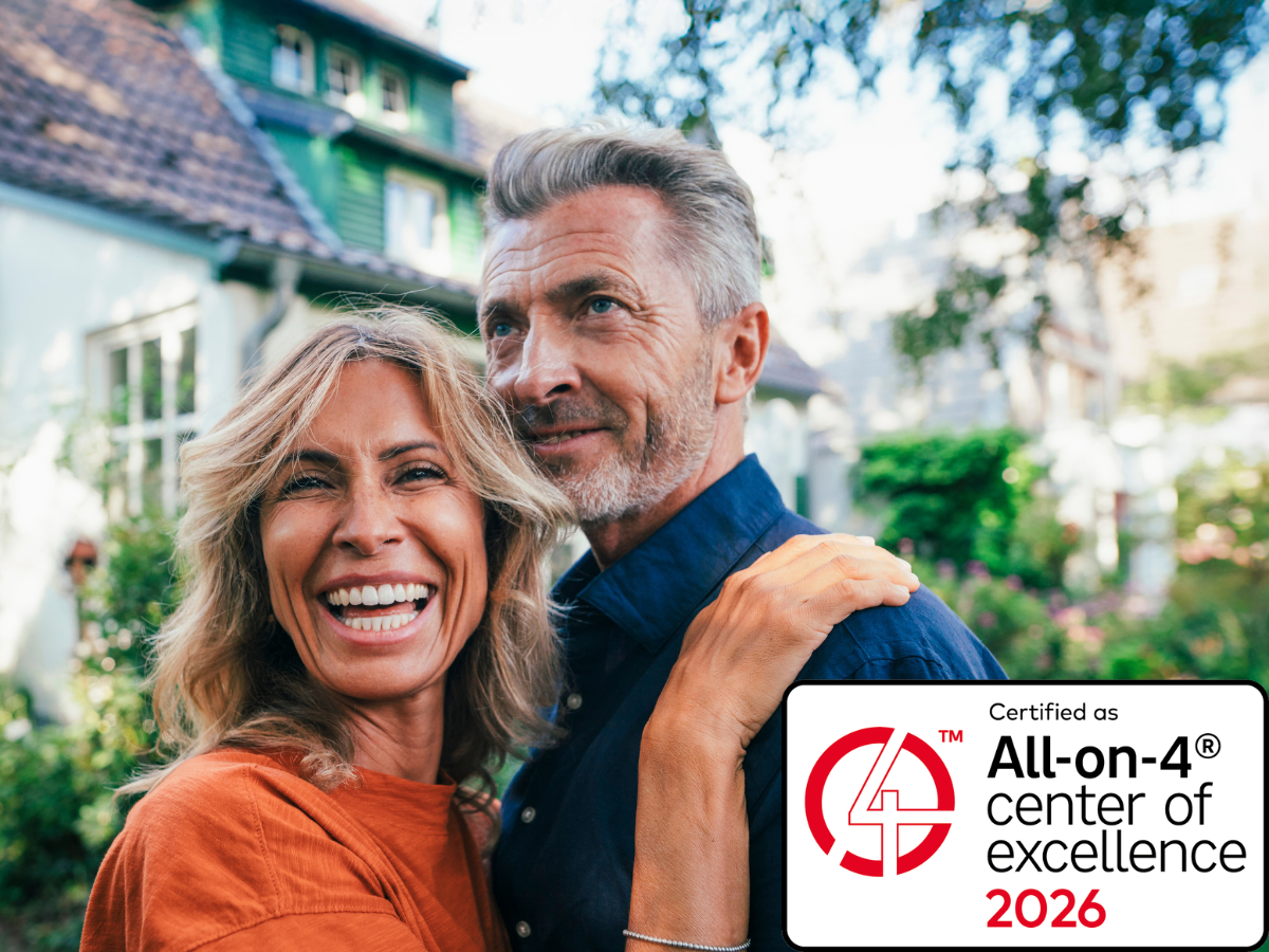 Ein lächelndes Paar mittleren Alters steht eng umschlungen im Garten vor einem Haus; unten rechts ist ein Siegel mit der Aufschrift „Certified as All-on-4® center of excellence 2026“ zu sehen.